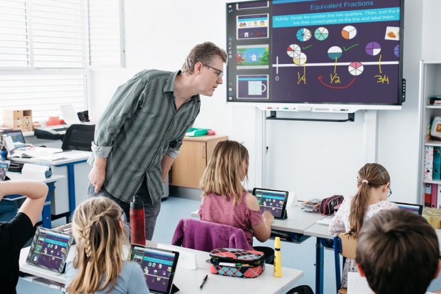 Teacher with SMART Board 7000 series using SMART's Software Learning Suite together with student devices within a classroom.